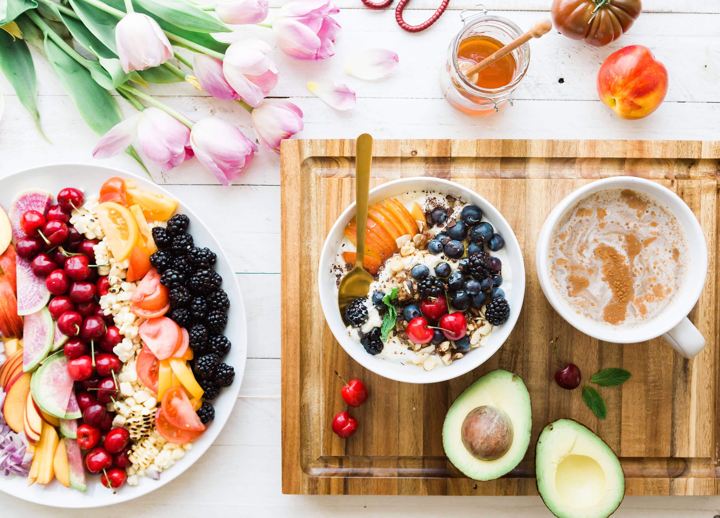 Several white plates and bowls on a table with vibrant colored sliced fruits and vegetables.