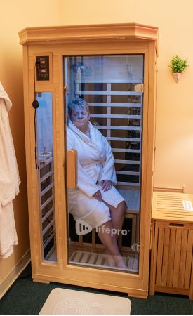 A woman in a white robe sitting in a infrared sauna.