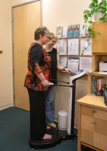 A woman standing on a body composition scale with her doctor standing nearby.